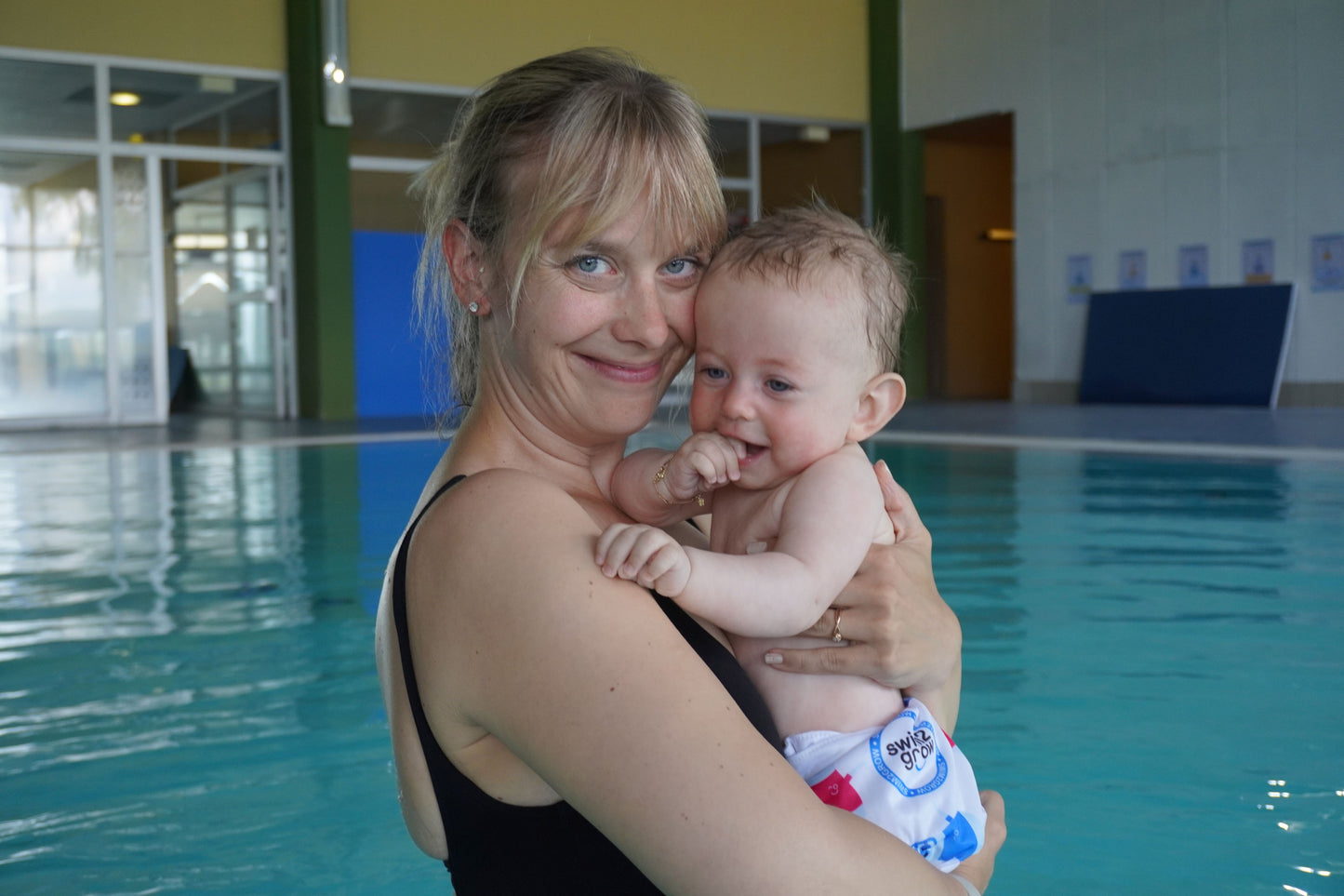 Mutter mit Baby im Arm, beide lachen, Baby trägt eine Schwimmwindel